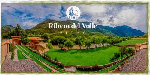 A serene countryside retreat featuring lush green lawns, rustic wooden structures, and majestic mountains under a vibrant sky, ideal for tranquil vacations in Pisac's Ribera del Valle.