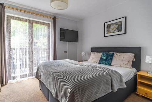 A cozy hotel room features a neatly made bed with soft bedding, a framed floral artwork on the wall, and a balcony view through sheer curtains, ideal for travelers seeking comfort and relaxation.