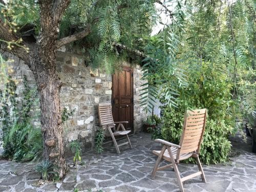 A serene stone courtyard with lush greenery, wooden chairs, and a rustic wooden door invites travelers to relax in a tranquil garden retreat.