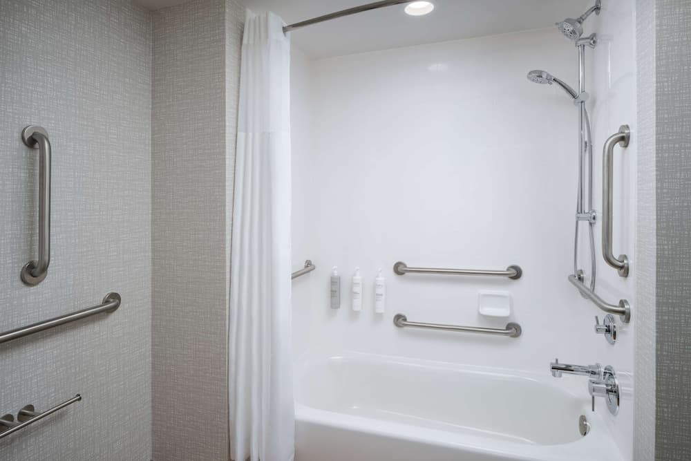 A clean, accessible bathroom with a bathtub featuring multiple grab bars, a shower curtain, and toiletries, ideal for travelers seeking comfort and safety in accommodations.
