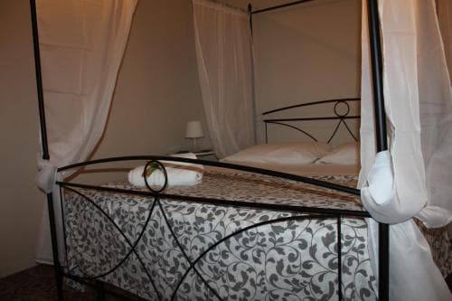 A cozy bedroom with a four-poster bed adorned with patterned linens and draped curtains creates an intimate atmosphere, ideal for travelers seeking a romantic getaway.
