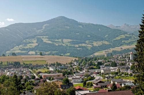 A serene mountain town nestled among lush green hills under a clear blue sky, ideal for travelers seeking a peaceful retreat with scenic views and quaint architecture.