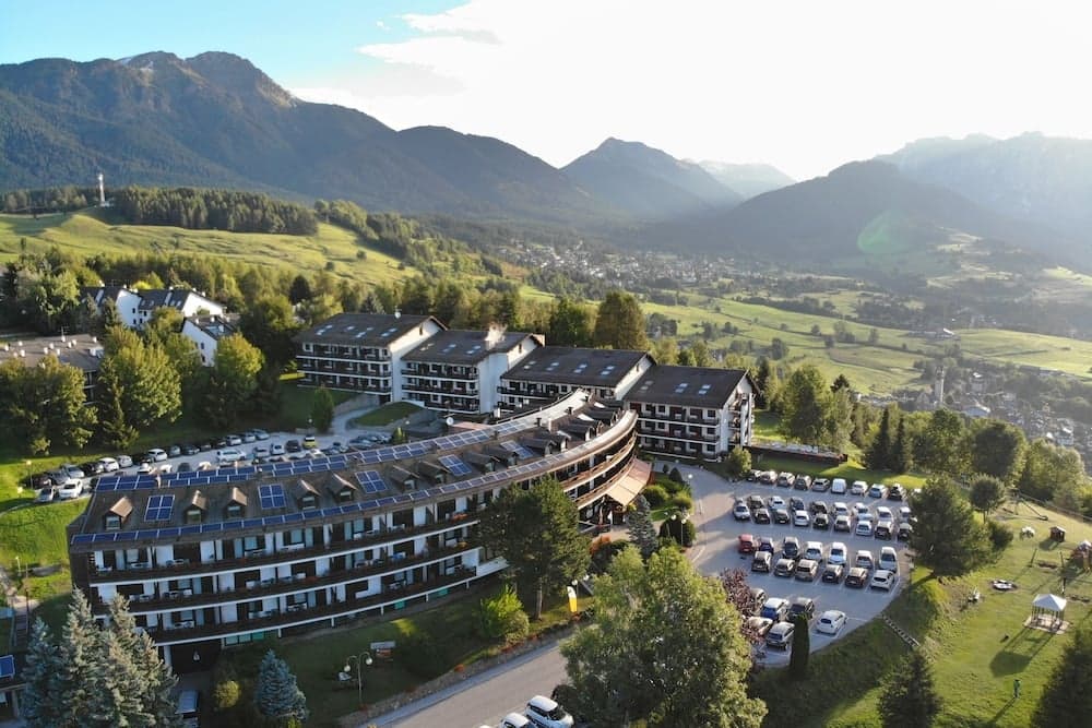 A serene mountain resort with solar-paneled roofs nestles amidst lush greenery and majestic peaks, offering travelers a tranquil escape with stunning views and eco-friendly accommodations.