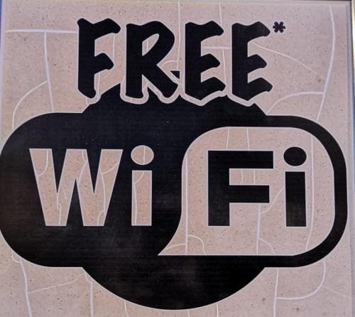A bold "FREE WiFi" sign on a textured wall invites travelers to connect in a welcoming urban setting, ideal for digital nomads seeking internet access.