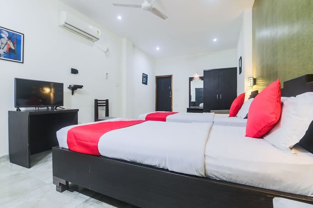 A cozy hotel room features two neatly made beds with red accents, a flat-screen TV, and modern amenities, ideal for travelers seeking comfort and convenience.