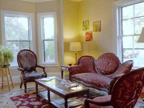 A cozy living room with vintage red upholstered furniture, a glass coffee table, and bright windows offers a charming retreat for travelers seeking a quaint and inviting accommodation.