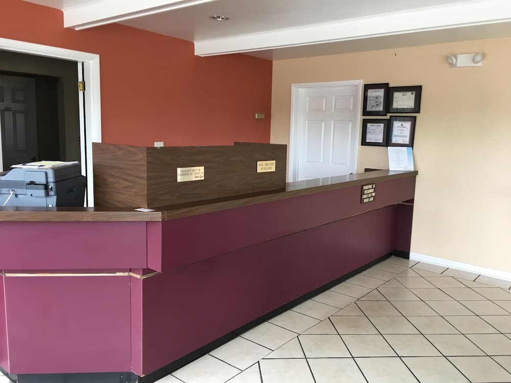 A cozy hotel reception area features a wooden desk with a printer, tiled flooring, and framed certificates on the wall, ideal for travelers seeking a welcoming check-in experience.