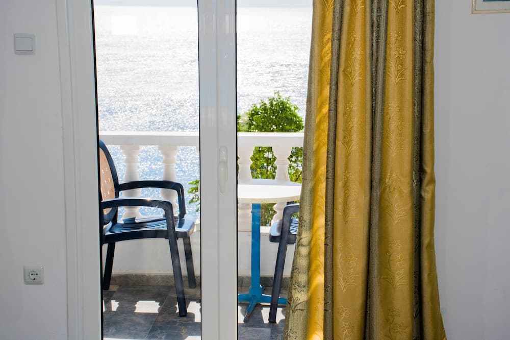 A serene coastal retreat features an inviting balcony with a white railing, black chairs, and a blue table, framed by golden curtains, perfect for travelers seeking relaxation by the sea.