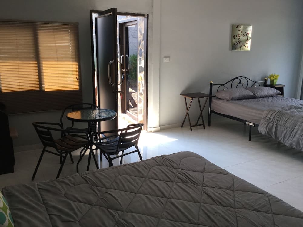 A cozy studio apartment features a simple bed setup, a small dining table by the window, and an open door leading to a sunny outdoor space, ideal for travelers seeking a comfortable and budget-friendly stay.