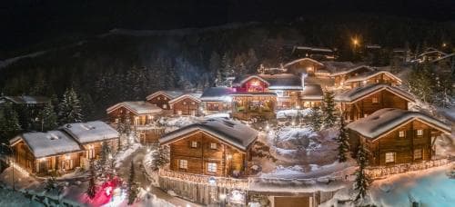 A cozy alpine village illuminated at night with snow-covered chalets and festive lights creates a magical winter retreat perfect for ski vacations.
