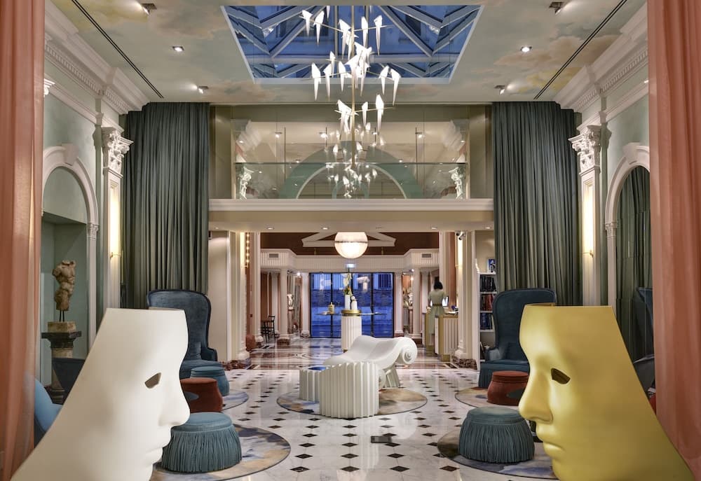 An opulent hotel lobby features a grand chandelier, luxurious face-shaped chairs, marble floors, and elegant curtains, creating an inviting atmosphere perfect for travelers seeking luxury accommodations.