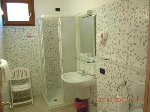 A cozy hotel bathroom features mosaic-tiled walls, a glass-enclosed shower, a white pedestal sink, and a small chair, ideal for travelers seeking comfort and functionality.