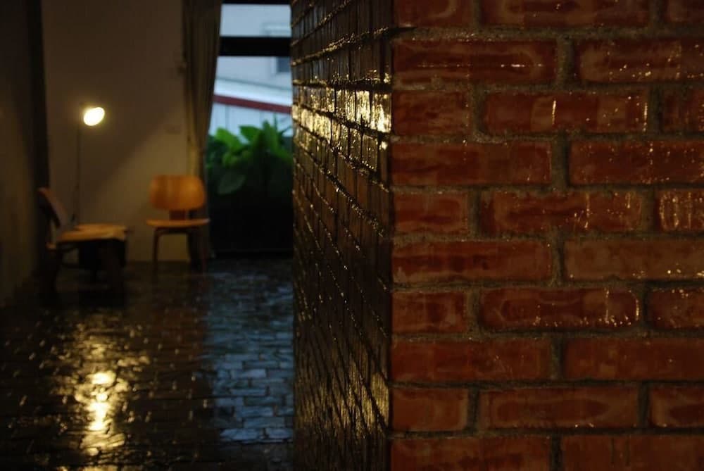 A cozy indoor space features a wet brick wall reflecting light, wooden stools, and a soft lamp glow, creating an intimate atmosphere ideal for travelers seeking a quiet retreat.