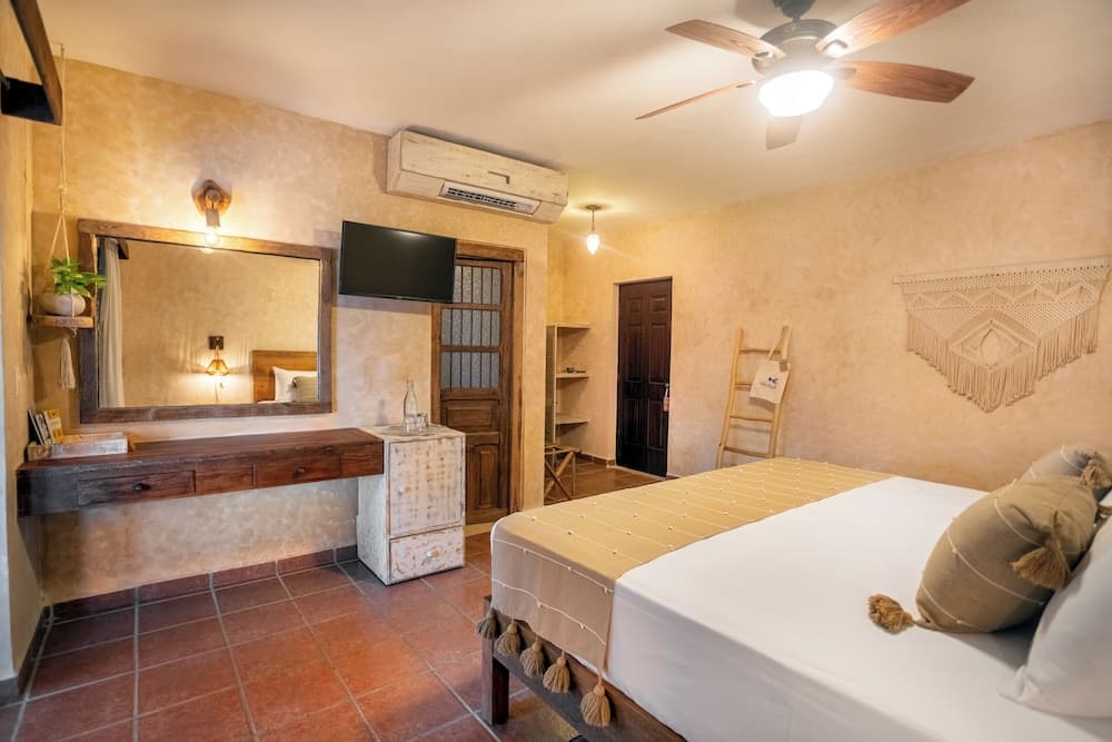 A cozy hotel room with warm-toned walls, tiled floors, a wooden vanity, and a bed adorned with tassels exudes a serene and inviting atmosphere, perfect for travelers seeking relaxation and comfort.