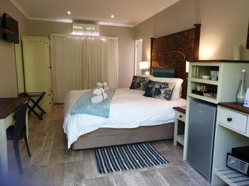 A cozy hotel room features a neatly made bed with patterned pillows, a small dining area, and a compact kitchenette, creating a welcoming atmosphere ideal for travelers seeking comfort and convenience.