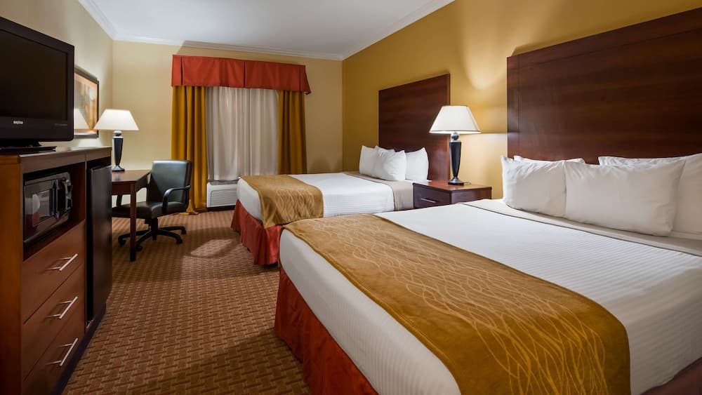 A cozy hotel room features two neatly made beds with warm-toned bedding, a desk with a chair, and a television cabinet, ideal for travelers seeking comfort and functionality during their stay.
