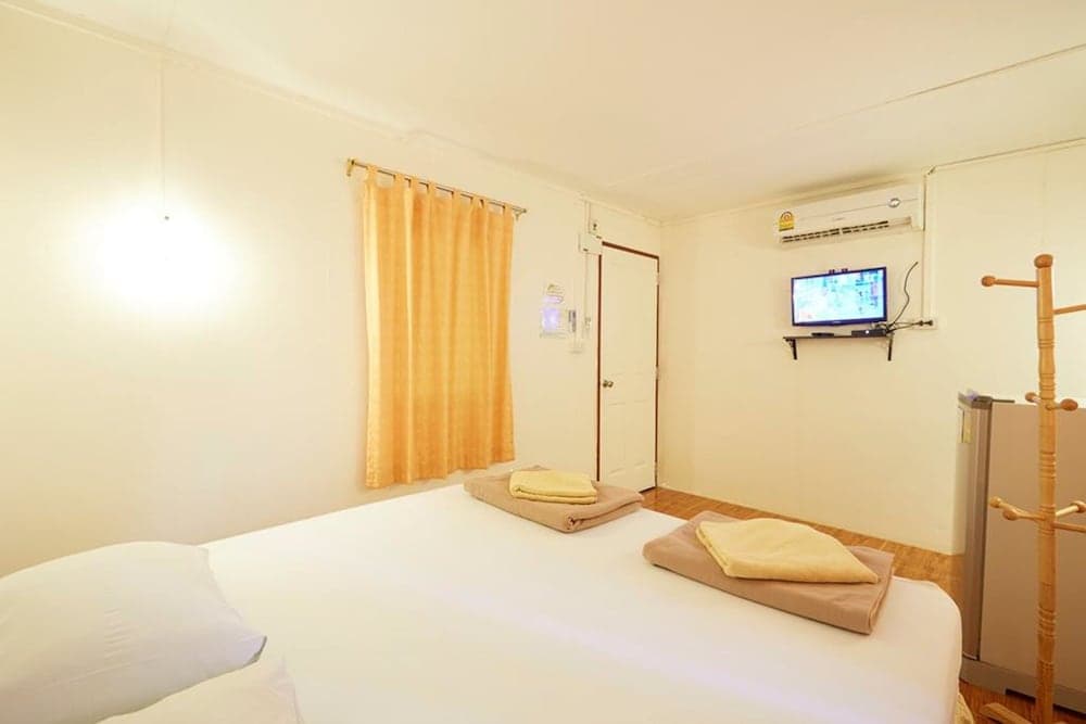 A cozy hotel room features a neatly made bed with folded towels, a mounted TV, an air conditioner, and wooden furnishings, ideal for travelers seeking comfort and simplicity.