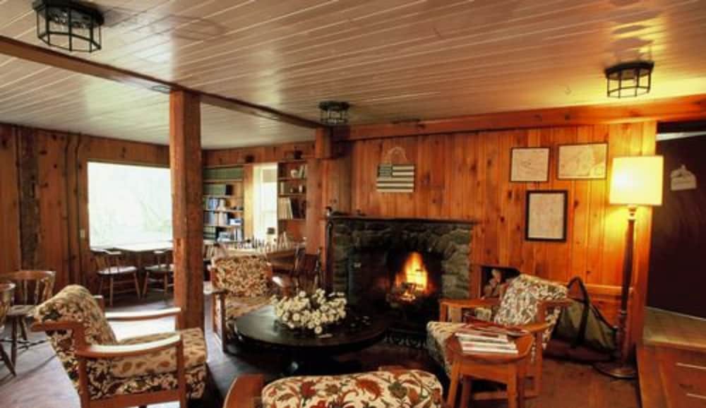A cozy cabin lounge with warm wooden interiors, a roaring fireplace, floral-patterned chairs, and soft lighting invites travelers seeking a serene retreat.