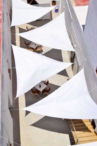 An inviting outdoor café shaded by white triangular sails creates a serene dining atmosphere, perfect for travelers seeking a relaxing spot to enjoy meals or drinks under the sun.