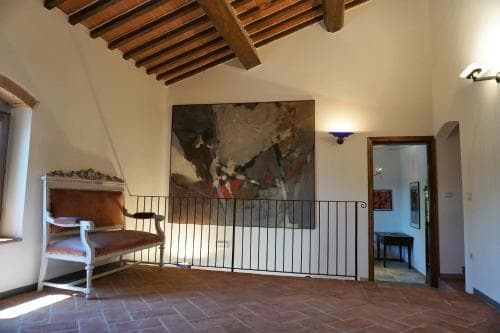 A cozy indoor space with rustic wooden beams, terracotta flooring, and a large abstract painting creates an inviting atmosphere in a historic villa, perfect for travelers seeking cultural immersion and relaxation.