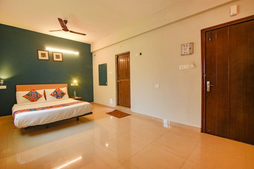 A cozy hotel room features a neatly made bed with colorful pillows against a teal accent wall, warm lighting, wooden doors, and tiled floors, ideal for travelers seeking comfort and simplicity.