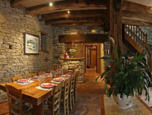 A cozy rustic dining area with stone walls, wooden beams, and a set table invites travelers to enjoy a warm meal in a charming countryside retreat.