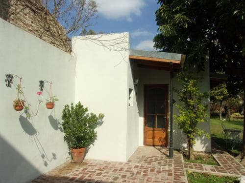 A serene courtyard entrance features a rustic brick pathway leading to a wooden door framed by greenery, ideal for travelers seeking a tranquil retreat in a cozy villa setting.