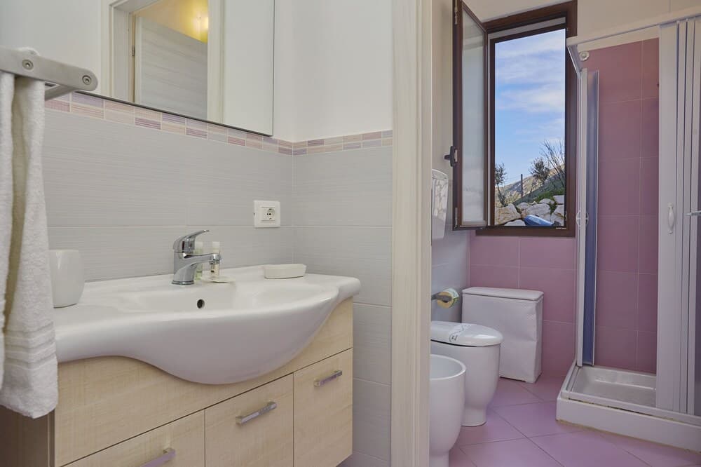 A cozy bathroom with a sink, toilet, shower, and a window offering a serene mountain view, ideal for travelers seeking relaxation in a private accommodation setting.