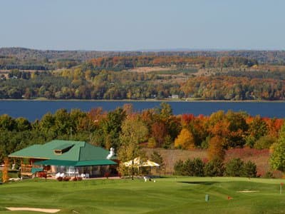 A serene golf course with vibrant autumn foliage overlooks a tranquil lake, featuring a clubhouse and umbrellas, ideal for leisurely getaways and scenic golfing experiences.
