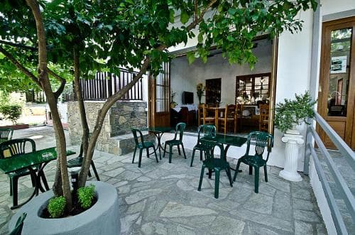 A serene outdoor café with stone-paved seating under lush greenery offers a tranquil spot for travelers to relax and enjoy meals in a cozy, rustic setting.
