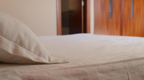 A cozy hotel room scene featuring a neatly made bed with soft beige linens, wooden closet doors in the background, evoking a calm and inviting atmosphere ideal for travelers seeking relaxation.