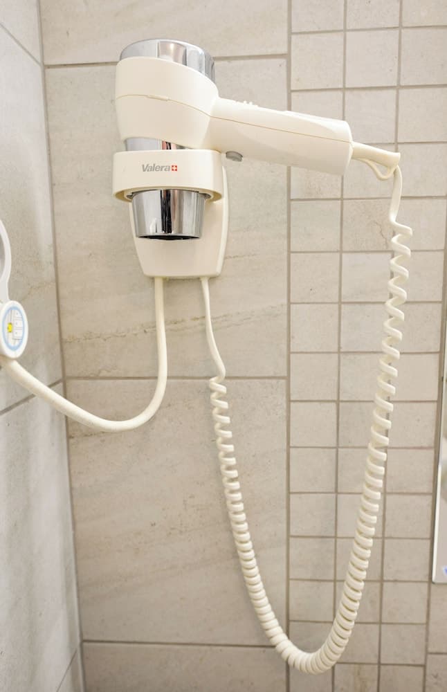 A wall-mounted Valera hairdryer with a coiled cord is neatly installed in a tiled bathroom, offering travelers a convenient amenity for personal grooming.