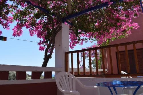 A serene balcony adorned with vibrant pink bougainvillea flowers offers a picturesque seaside view, perfect for relaxing with a cup of coffee during a tranquil vacation getaway.