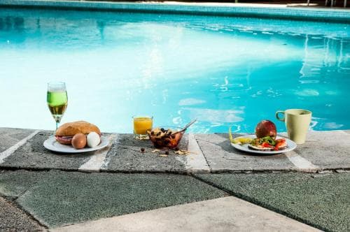 A serene poolside setting features a delightful breakfast spread with fresh fruits, pastries, and beverages on stone tiles, perfect for a relaxing morning getaway.