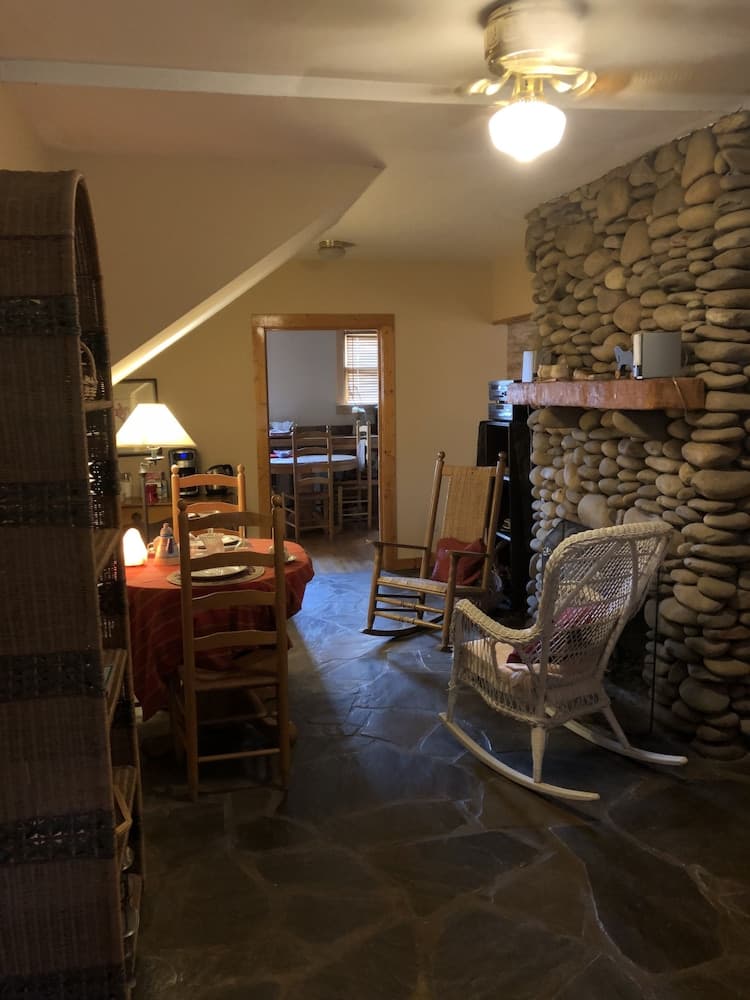 A cozy cabin interior features a stone fireplace, wooden rocking chairs, and a dining area with warm lighting, ideal for a relaxing getaway.