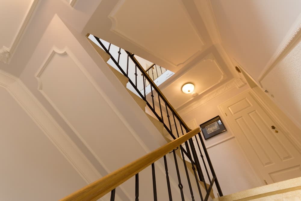 An elegant indoor staircase with ornate white paneling, a wooden handrail, black iron balusters, and soft lighting creates a sophisticated atmosphere ideal for luxury home tours or real estate photography.