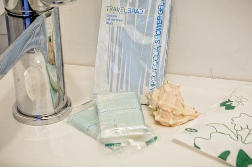 A serene bathroom countertop displays travel-sized toiletries, a seashell, and a soap dispenser, ideal for travelers seeking compact essentials in a clean and organized setting.
