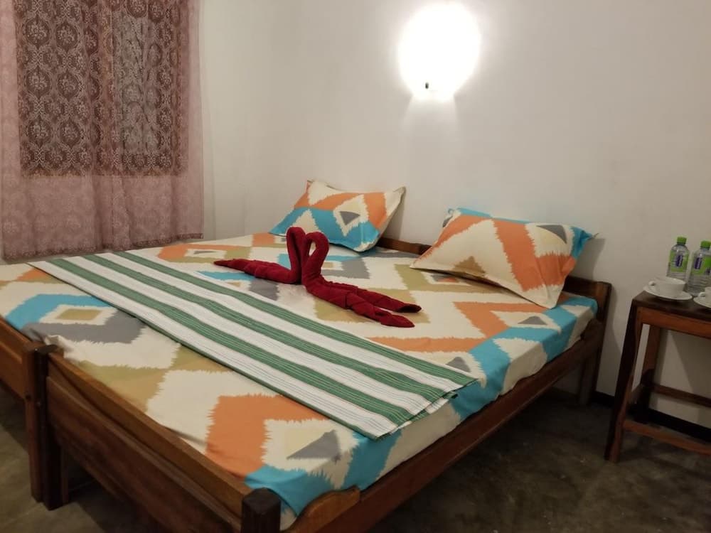 A cozy bedroom with a wooden bed adorned in colorful geometric bedding, a small side table with tea cups and water bottles, and soft lighting creates an inviting atmosphere ideal for travelers seeking comfort and relaxation.