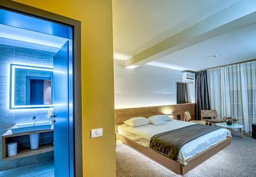 A cozy hotel room features a neatly made bed beside a modern bathroom with blue lighting, ideal for travelers seeking comfort and style in their accommodations.