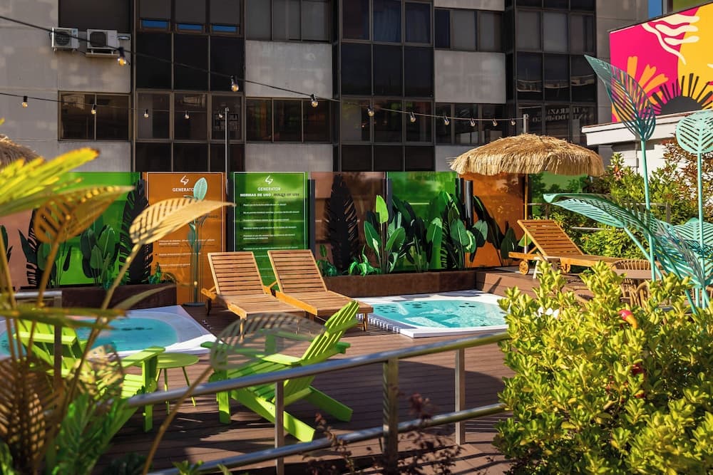A vibrant rooftop terrace features colorful lounge chairs, tropical plants, and a small pool, creating a relaxing urban oasis ideal for city travelers seeking a refreshing retreat.