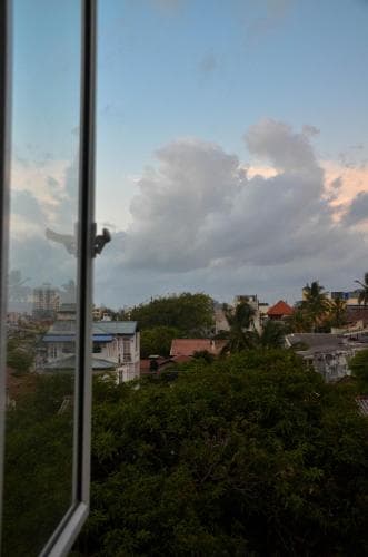 A serene urban landscape viewed through a window at dusk, featuring lush greenery, scattered rooftops, and a dramatic sky, ideal for travelers seeking tranquil cityscapes.