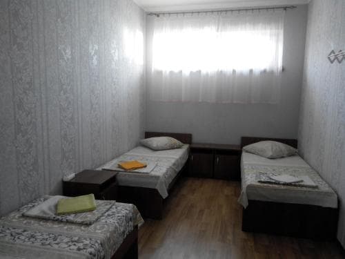 A cozy budget-friendly guesthouse room features three neatly arranged single beds with patterned bedding under soft natural light from a curtained window, ideal for travelers seeking simple accommodations.