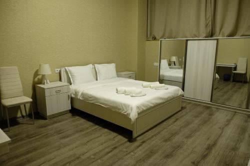 A cozy hotel room features a neatly made bed with white linens, wooden flooring, a mirrored wardrobe, and simple furnishings, ideal for travelers seeking comfort and functionality.