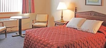 A cozy hotel room features a neatly made bed with red bedding, a warm lamp, and comfortable seating by the window, ideal for travelers seeking relaxation and convenience.