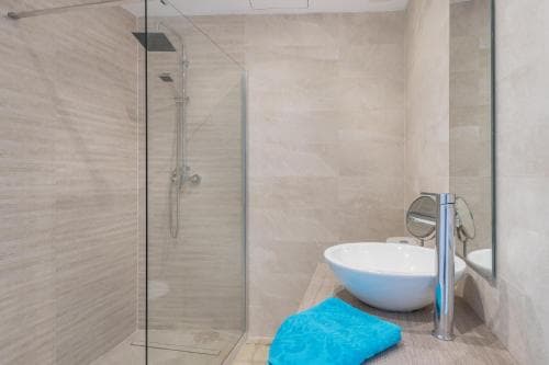 A modern bathroom with beige tiled walls, a glass-enclosed shower, a sleek white vessel sink, and a blue towel adds a serene and luxurious touch, ideal for travelers seeking comfort in upscale accommodations.