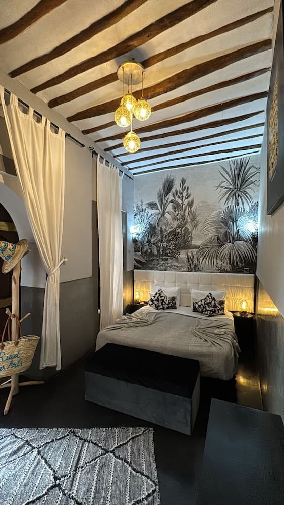A cozy bedroom with exposed wooden beams, tropical wall mural, and warm lighting creates an inviting atmosphere, perfect for travelers seeking a unique and relaxing retreat.