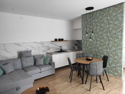 A cozy modern apartment features a stylish living area with a gray sofa, wooden dining set, and vibrant wallpaper, ideal for travelers seeking comfort and design in urban accommodations.