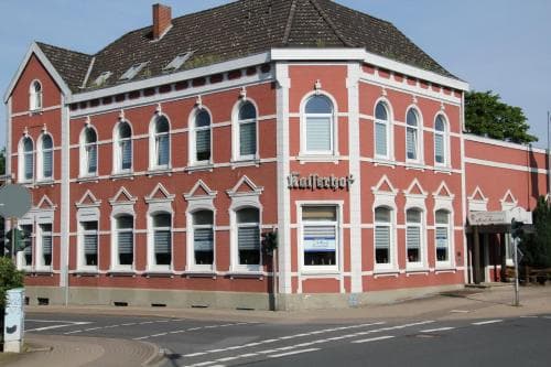 A charming red-brick building with arched windows and a quaint signboard stands at a quiet street corner in a European town, ideal for travelers seeking a cozy accommodation or local history exploration.