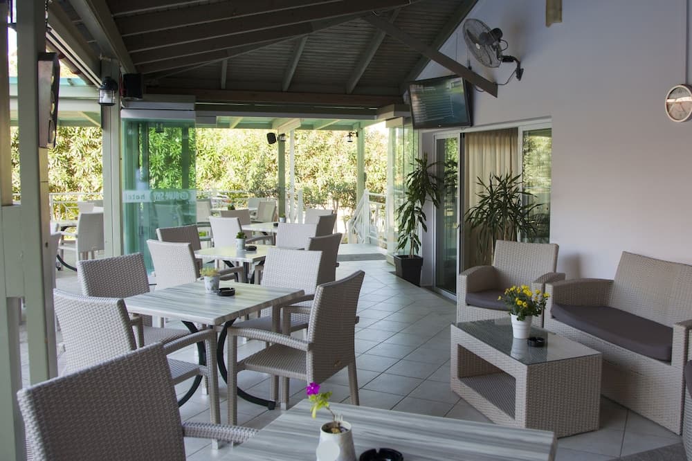 A serene outdoor café with wicker furniture, potted plants, and lush greenery offers a relaxing spot for travelers to unwind and enjoy refreshments.