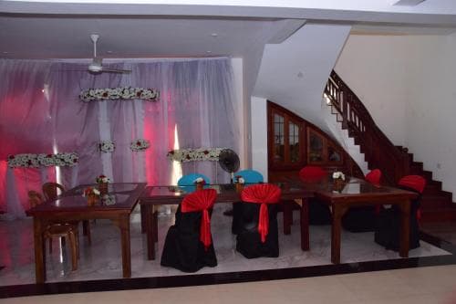 A warmly lit indoor event space features tables adorned with red bows and floral arrangements against a draped backdrop, ideal for intimate gatherings or small celebrations.